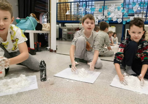 Uczniowie klasy 3 robiący śnieg. Jeden z chłopców trzyma w ręku płyn do mycia naczyń, obok stoi pianka do golenia.
