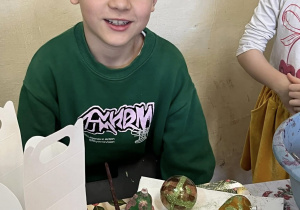 Chłopiec przy stoliku. przed nim ozdobione własnoręcznie bombki.