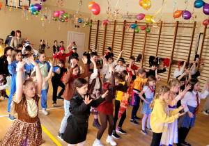 Dzieci z uniesionymi rękami w tańcu. Nad nimi rozwieszone balony i serpentyny.