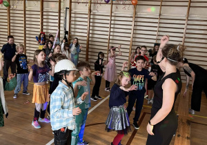 Dzieci w karnawałówych strojach zgromadzone przed animatorką w czasie tańca.