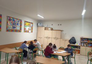 Uczniowie klasy 5 siedzący w grupach przy stolikach pracujący nad projektem.