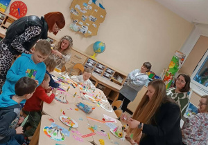 Dzieci zgromadzone wokół stołu, na którym wyłożone sa masteriały plastyczne i kreatywne do tworzenia wiosennych kapeluszy.