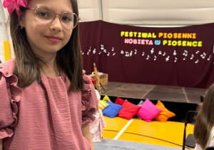 Uczennica klasy 3a pozująca do zdjęcia, w tle dekoracja z napisem Festiwal Piosenki o Kobiecie.