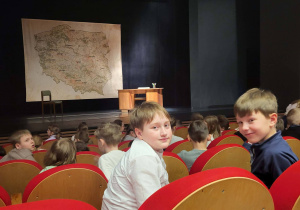 Dwaj chłopcy siedzący na widowni, w tle scena z rekwizytami i pozostali widzowie.