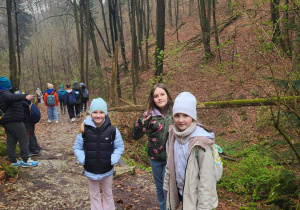 Na pierwszym planie trzy dziewczynki, w tle pozostałe dzieci spacerujące leśną ścieżką po Ojcowskim Parku Narodowym.