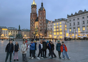 Wieczorna sceneria Starego Miasta w Krakowie i grupka uczniów pozująca na tle Kościoła Mariackiego.