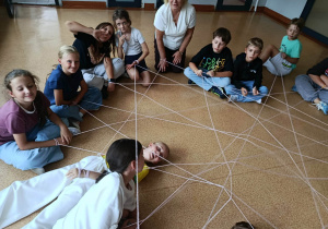 Grupa uczniów w kręgu tworząca sieć z trzymanej w rękach włóczki.