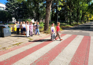 Uczniowie przechodzący parami przez jezdnię, stosując zasady bezpieczeństwa.
