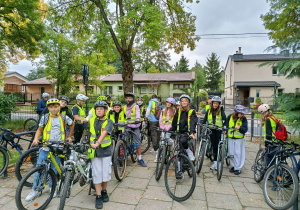 Uczniowie klasy 6 w odblaskowych kamizelkach z rowerami, zgromadzeni przed szkołą.