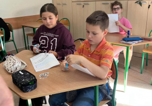 Dzieci siedzące w ławkach i wycinające elementy w kartach pracy.