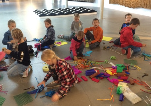 Dzieci siedzące na podłodze z kolorowymi przyborami do pracy.
