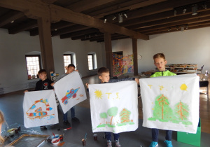 Czterech chłopców prezentuje swoje prace wykonane farbami na tkaninie.